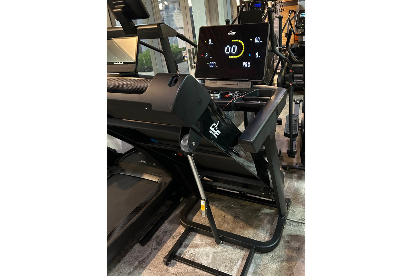 Black folding treadmill with digital display showing speed and power metrics, metal frame and black running belt in showroom 