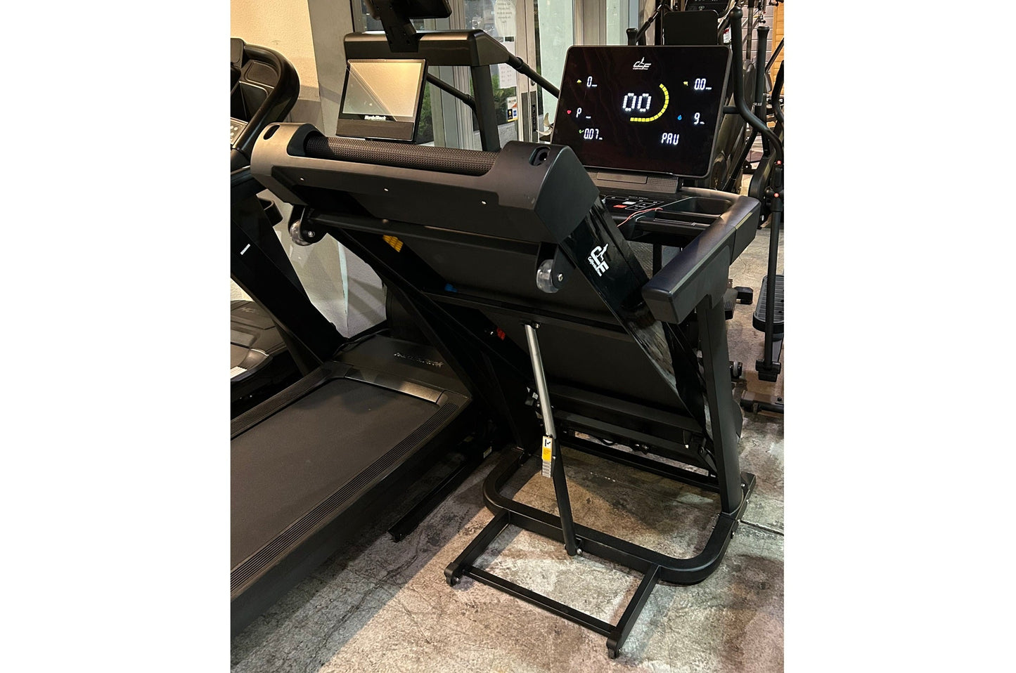 Black folding treadmill with digital display screen, cushioned running deck, and black frame on showroom floor