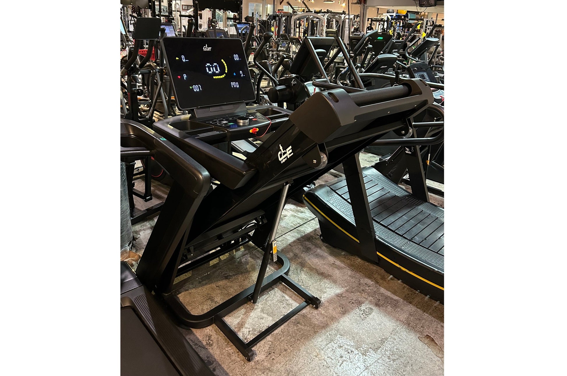 Black folding treadmill with digital display console and yellow accents, shown in gym setting