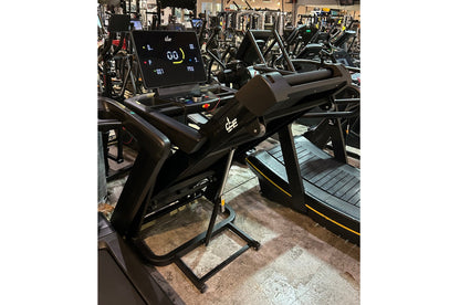 Black folding treadmill with digital display console and yellow accents, shown in gym setting