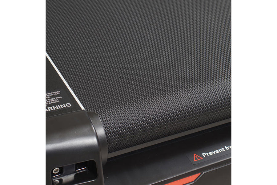 Close-up of black textured treadmill belt and frame showing motor housing and safety warning label