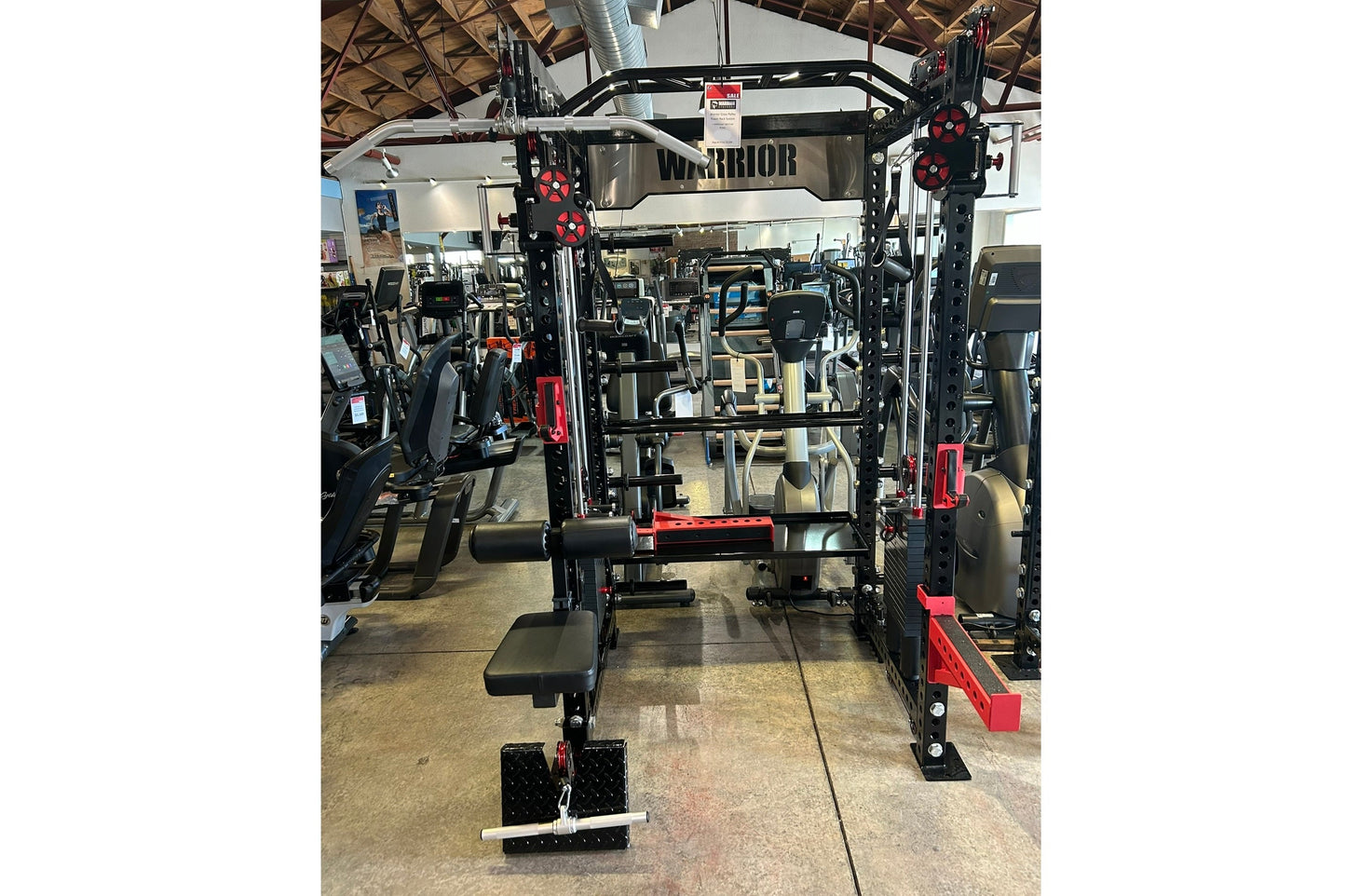 Warrior cable crossover power rack with dual black uprights, red accents, adjustable pulleys, lat pulldown attachment, and we