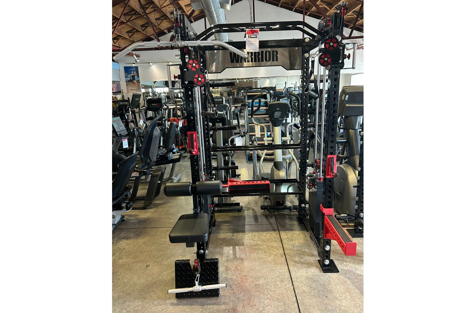 Warrior cable crossover power rack with dual black uprights, red accents, adjustable pulleys, lat pulldown attachment, and we