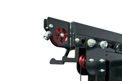 Black steel cable crossover pulley system with red wheels and metal bolts, mounted on white background