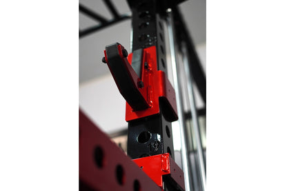 Red and black cable crossover pulley attachment with grip handles on gym power rack frame