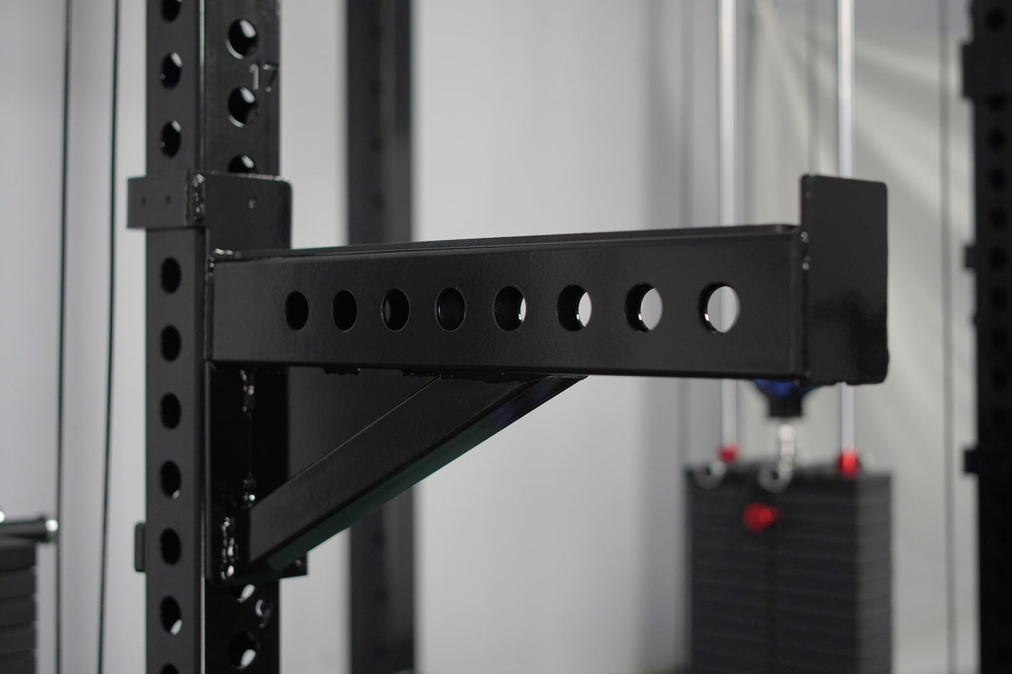 Black steel cable crossover arm with eight circular pulleys attached to vertical rack frame with angled support bracket