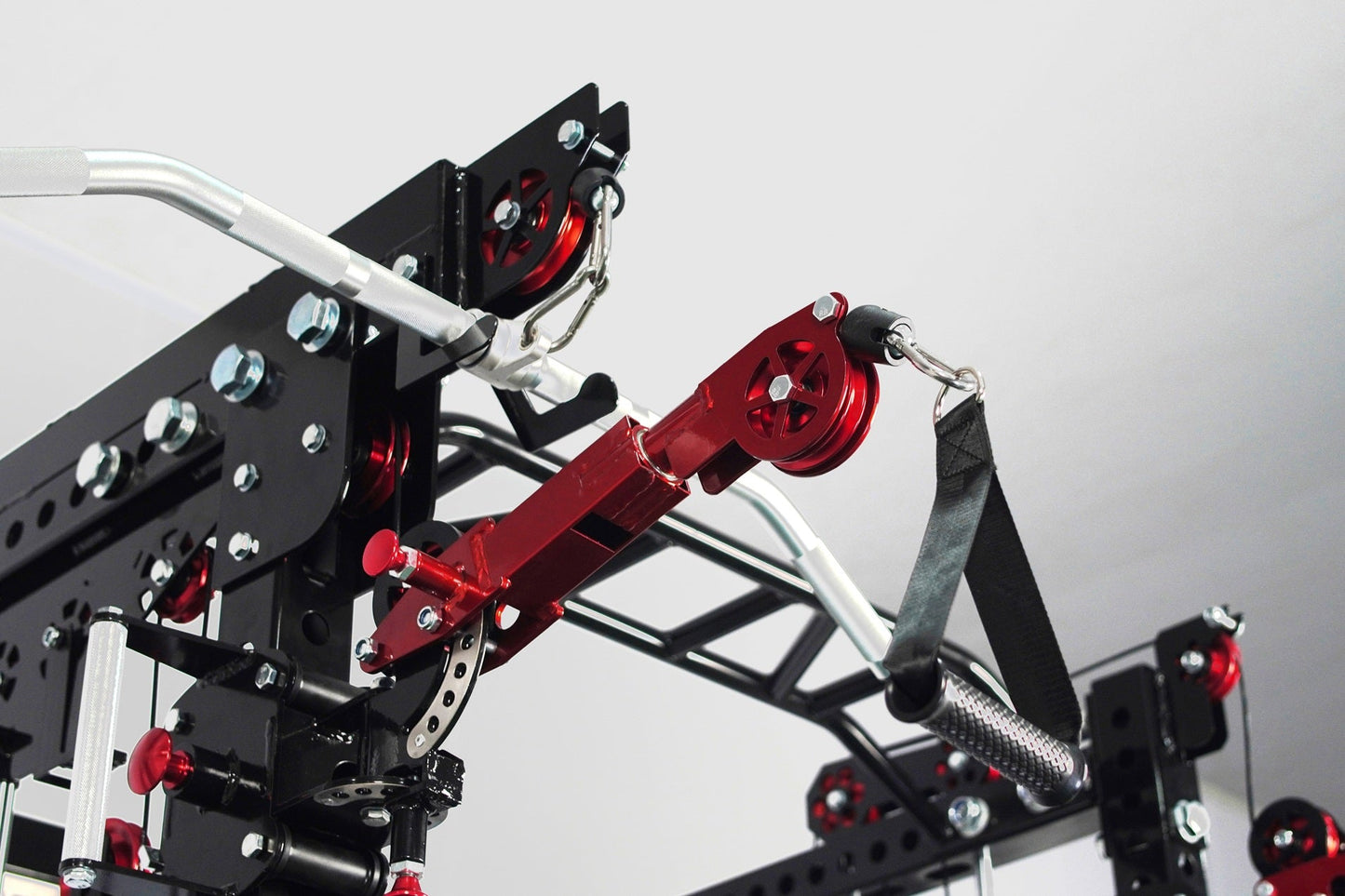 Black and red cable crossover pulley system with silver aluminum frame, dual adjustable pulleys, and black straps on white ba